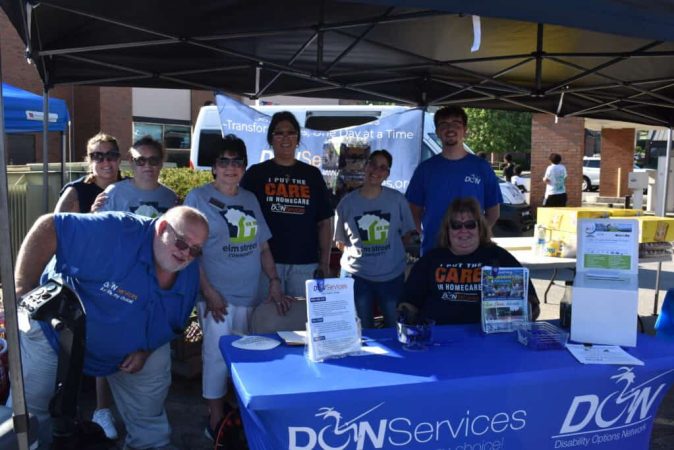 Group of volunteers at DON Services booth during community event.
