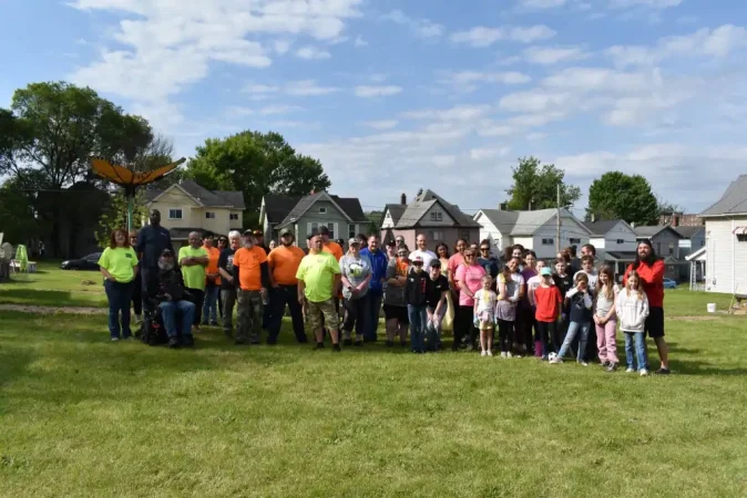 Group of people gathered outdoors on a grassy field with houses in the background.