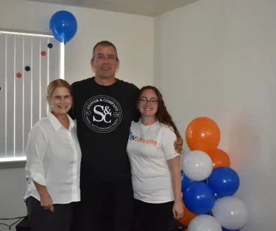 Group of three people celebrating with balloons at DON Services event.