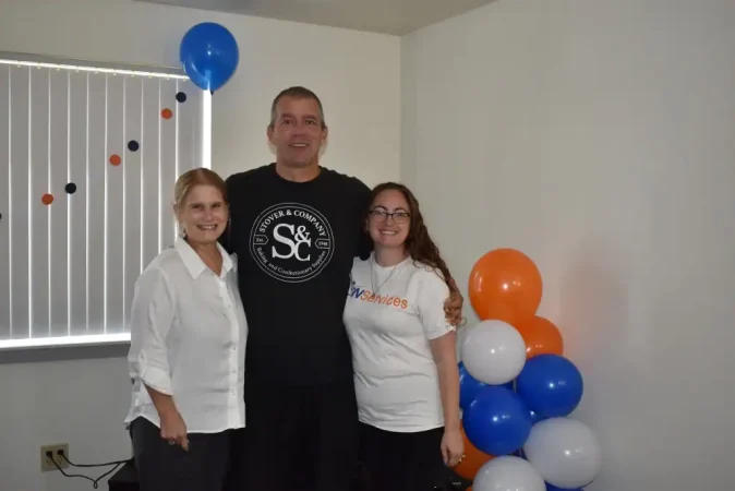 Group of three people celebrating with balloons at DON Services event.