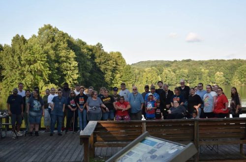 DON Services Group Photo at DON Fishing Derby Group photo of DON Services team outdoors near a lake with trees and hills.